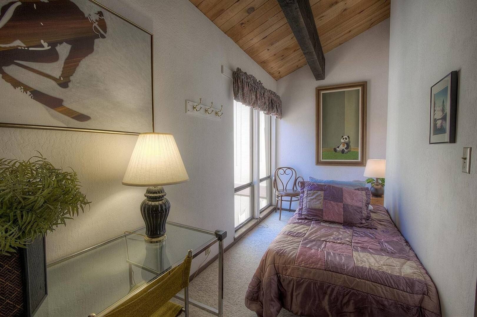 A bedroom with a bed, a chair, a table with a lamp, a window, and a painting on the wall.