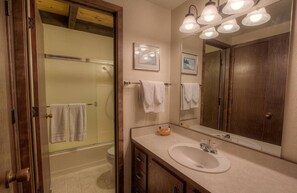 A bathroom with a glass shower door, a sink with a mirror, and a wooden vanity.