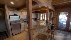 A kitchen with wooden cabinets, a stainless steel refrigerator, granite countertops, and a large island with bar stools. - The Bass Chalet 3 Bedroom Home by RedAwning (Kings Beach)