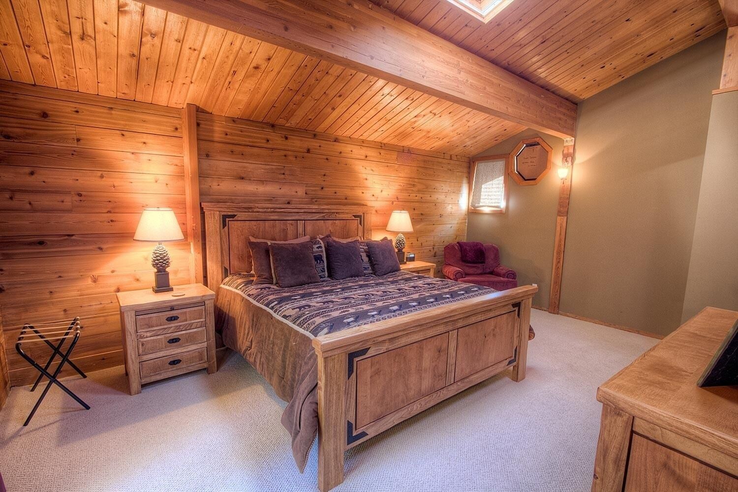 Ein gemütliches Schlafzimmer aus Holz mit einem großen Bett, zwei Nachttischen mit Lampen, einem roten Sessel und einem kleinen Holzschrank.