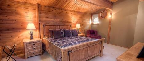 Ein gemütliches Schlafzimmer aus Holz mit einem großen Bett, zwei Nachttischen mit Lampen, einem roten Sessel und einem kleinen Holzschrank.