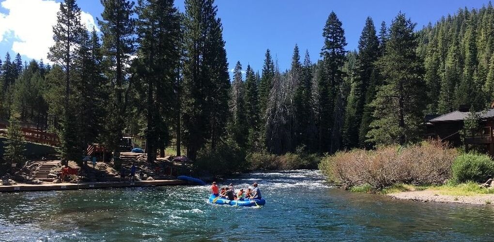 Una balsa con gente navegando por un río rodeado de bosque denso.