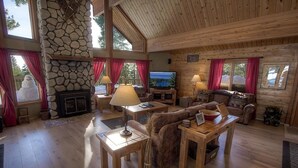 A cozy cabin interior with a stone fireplace, wooden furniture, and large windows. - The Bass Chalet 3 Bedroom Home by RedAwning (Kings Beach)