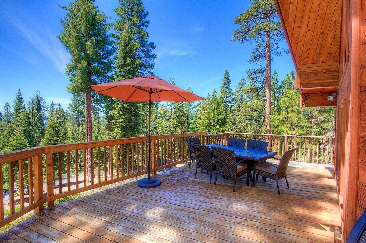 Eine Holzterrasse mit Tisch und Stühlen, umgeben von einem Holgitter, mit Blick auf einen Wald.