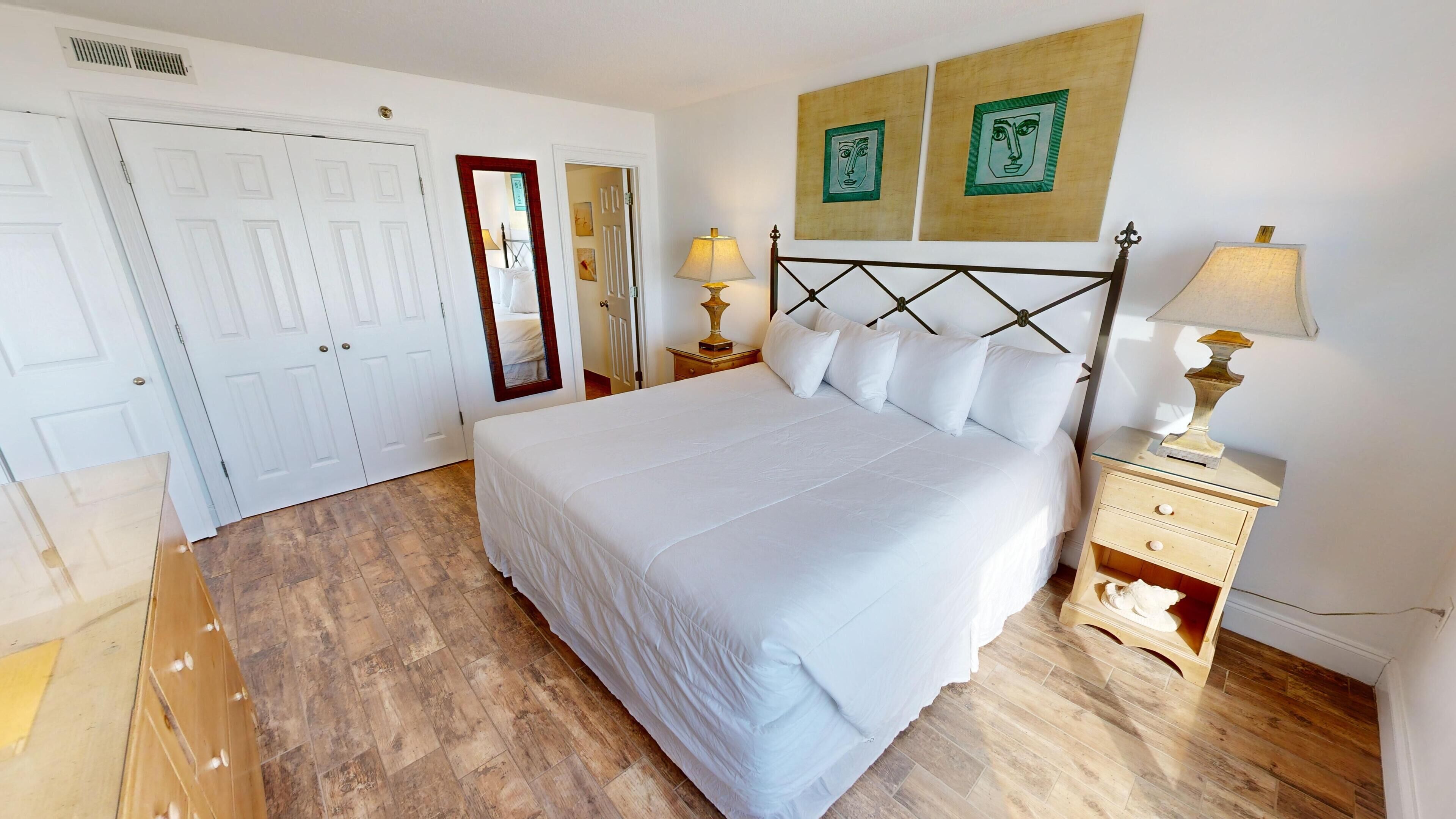Une chambre à coucher bien aménagée, avec un grand lit, deux tables de chevet avec des lampes, une armoire et deux œuvres d’art encadrées accrochées au mur.