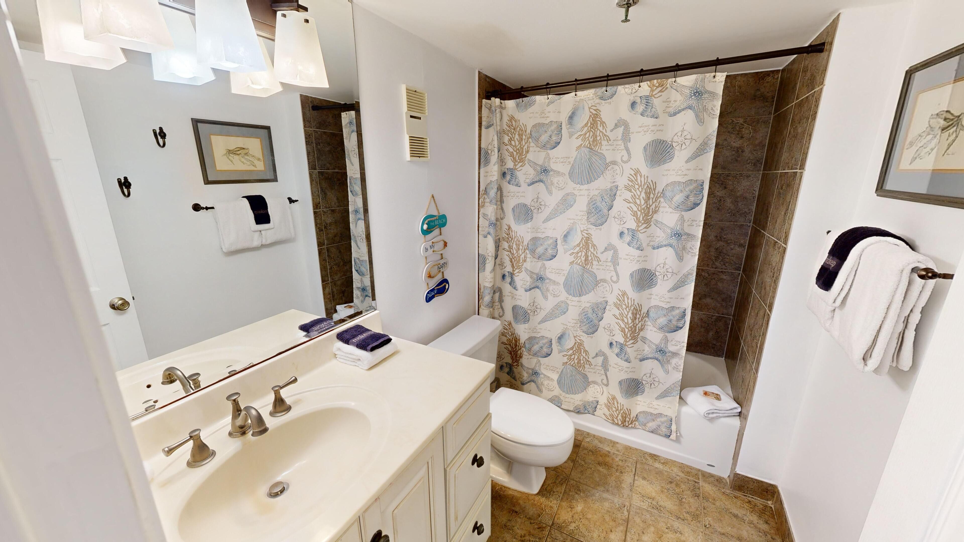 A bathroom with a white sink, vanity, and toilet. There is a shower curtain with a sea-themed pattern.