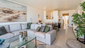 En moderne stue med en hvid sofa, et glasbord og et stort abstrakt maleri.