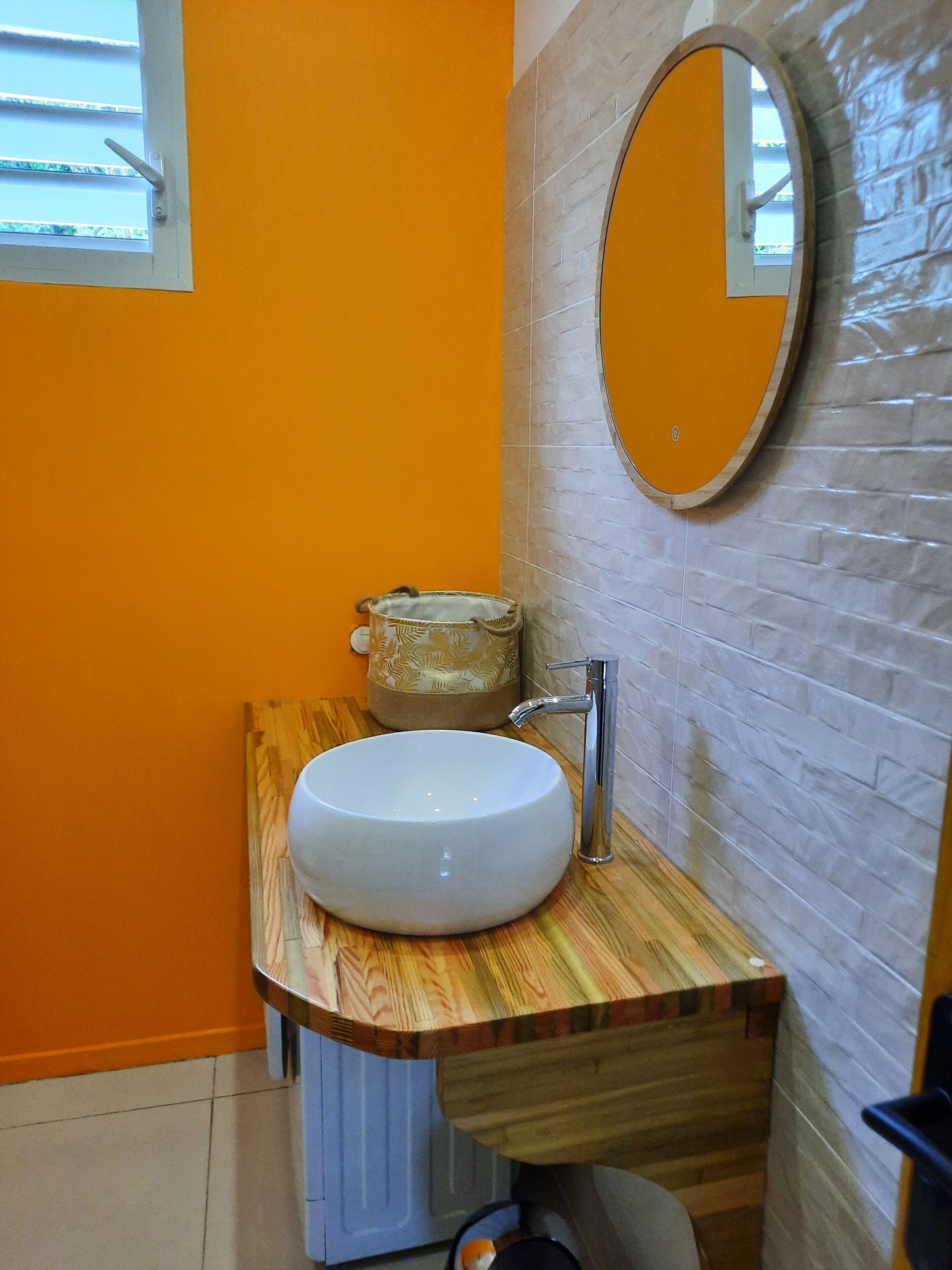 A bathroom with a white sink, a wooden vanity, a mirror, and a window.