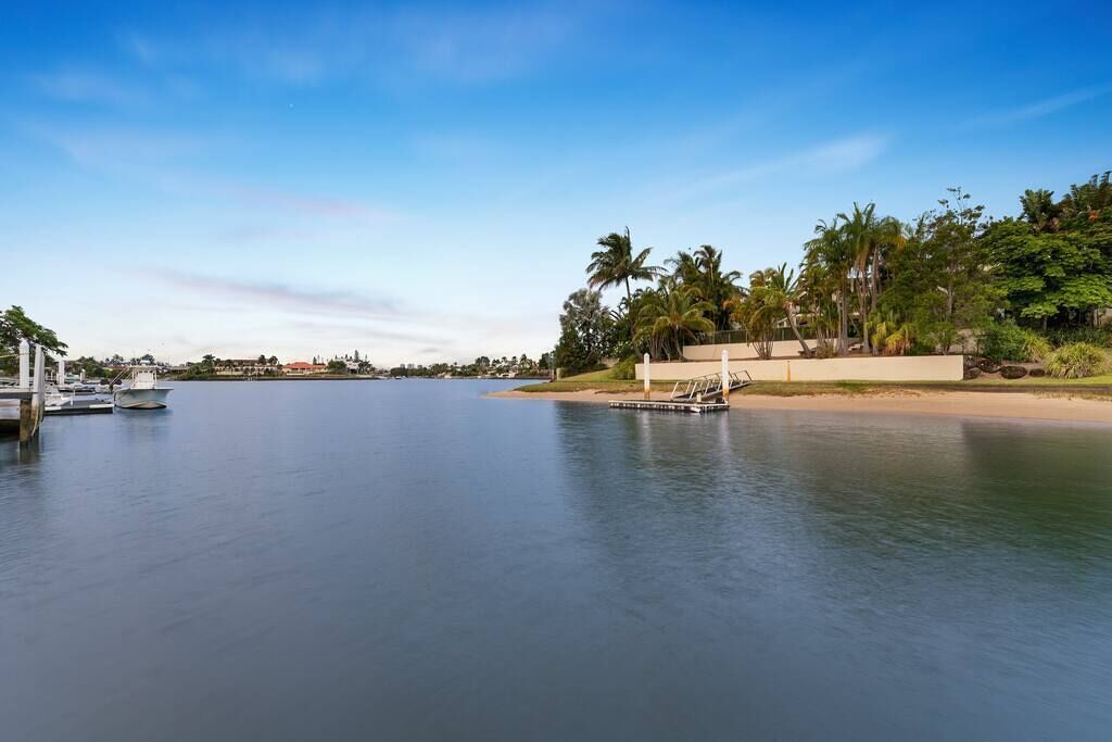 A calm waterfront with a dock, boats, and a sandy beach with palm trees.