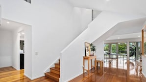 Une pièce spacieuse avec un plancher en bois, un escalier blanc et une vue sur l’extérieur.