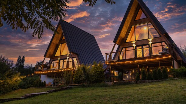 A modern, triangular-shaped building with large windows and a balcony, surrounded by greenery. - Three-Bedroom A Frame Chalet in Dealu Mare (Malu Roșu)