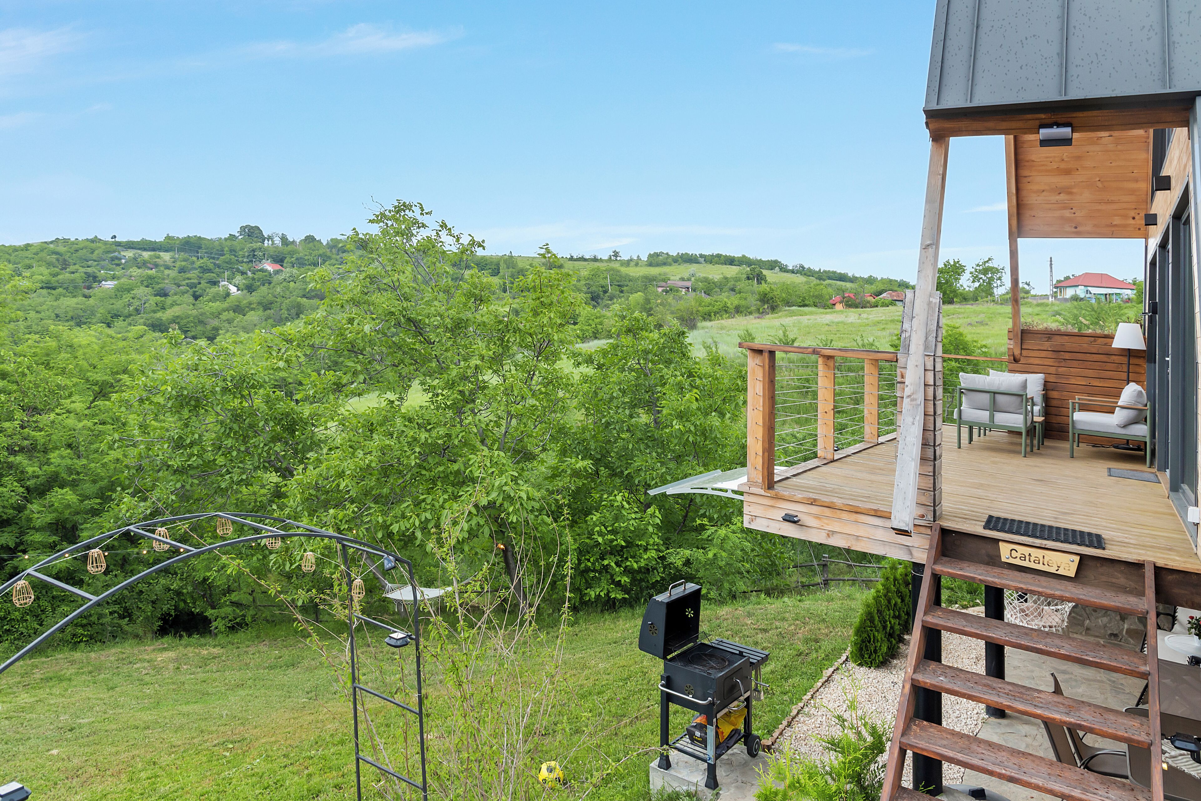 A deck with outdoor furniture, a grill, and a view of a green landscape.