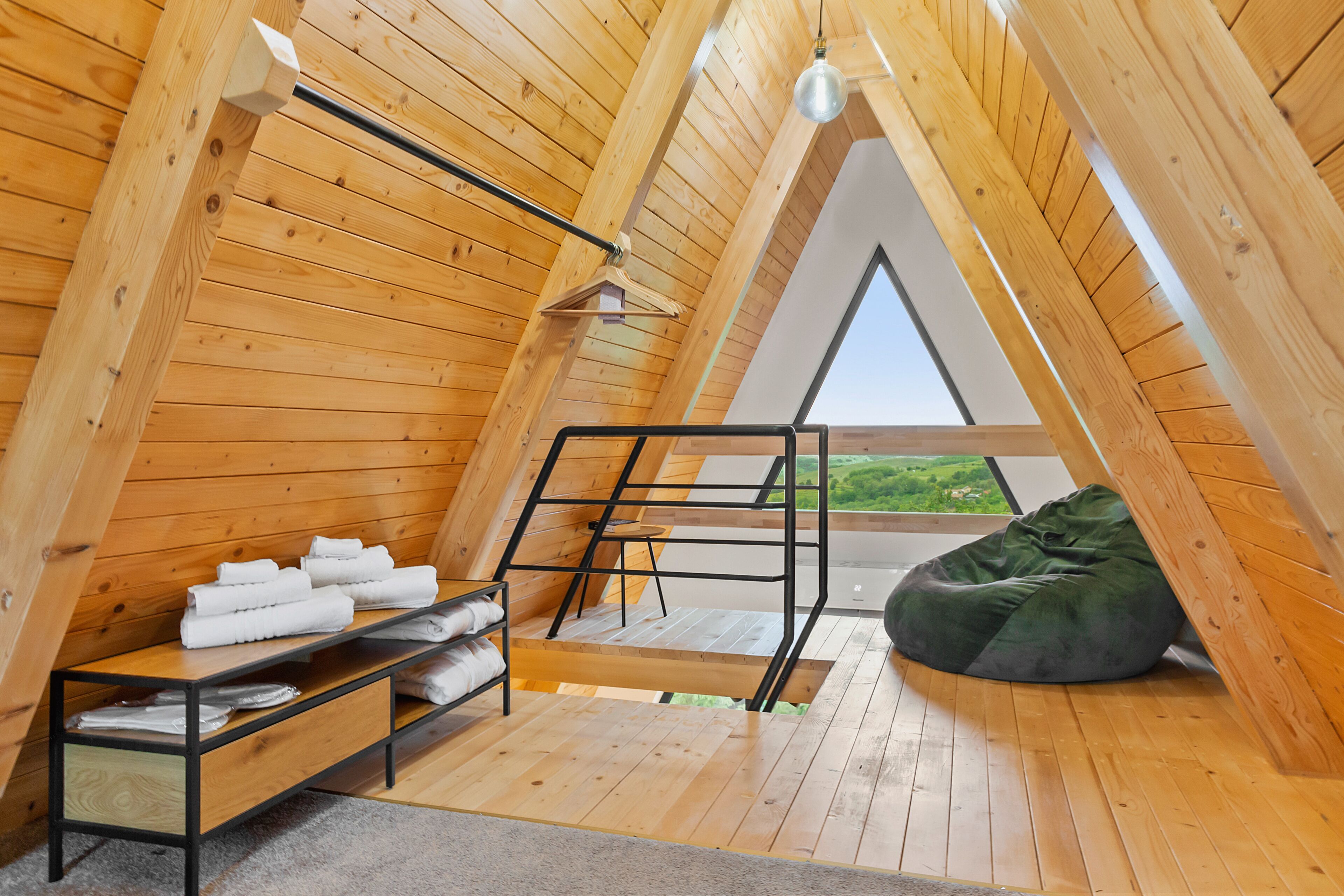 A wooden attic room with a loft bed, a bean bag, and a small table with towels.