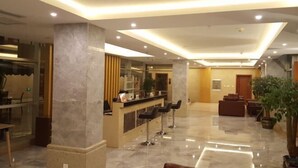 A modern lobby with a reception desk, bar stools, seating area, and a large potted plant. - Jiaozishan Resort Hotel (Luquan)