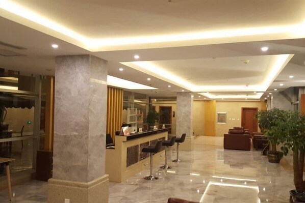 A modern lobby with a reception desk, bar stools, seating area, and a large potted plant. - Jiaozishan Resort Hotel (Luquan)