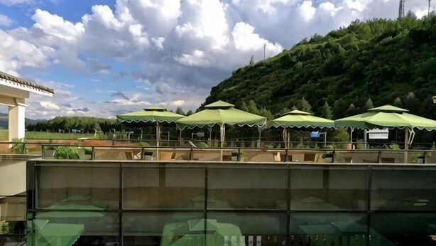 A restaurant with outdoor seating, green umbrellas, and a view of a hillside. - Jiaozishan Resort Hotel (Luquan)