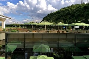 A restaurant with outdoor seating, green umbrellas, and a view of a hillside. - Jiaozishan Resort Hotel (Luquan)