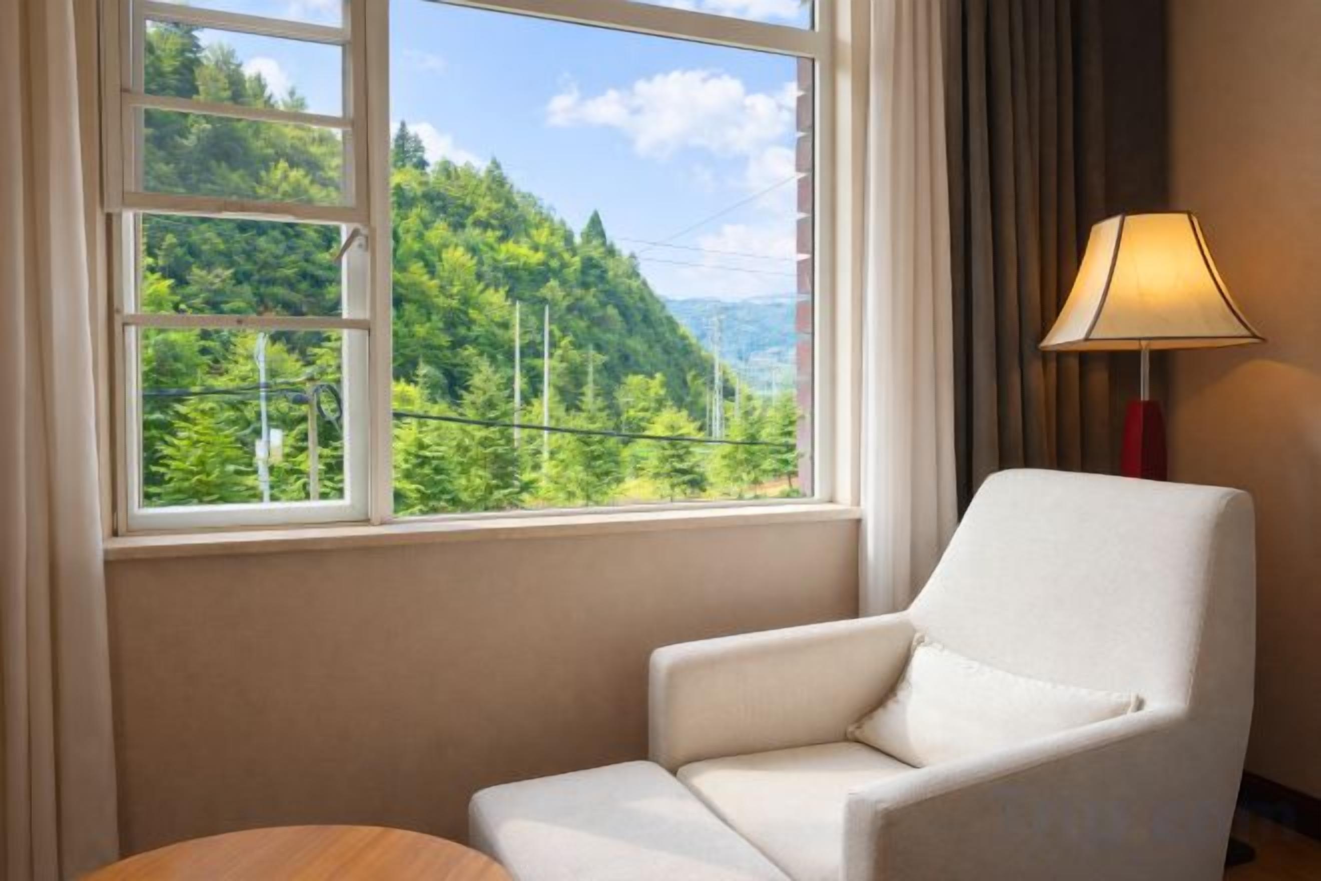 Una habitación con un sillón blanco, una mesa redonda pequeña y una ventana que da a un paisaje verde.