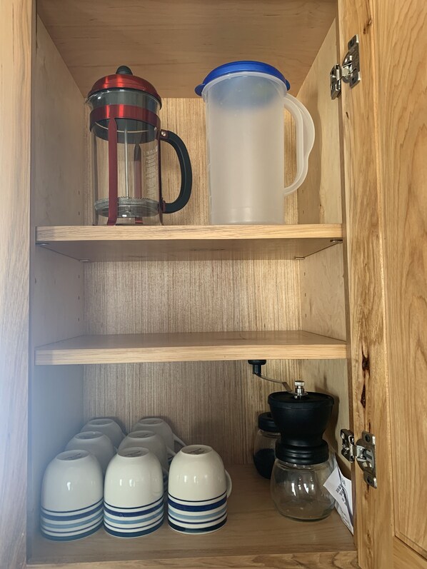 A wooden cabinet with shelves holding a coffee maker, a pitcher, and several white mugs with blue stripes. - Wind River Tiny Home ~ Adventures await Yellowstone Tetons Fly Fishing (Daniel)