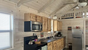 A kitchen with wooden cabinets, a microwave, a stove, a refrigerator, and a ceiling fan.