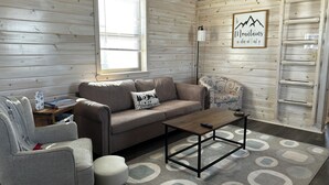 A cozy room with a sofa, armchair, and ottoman, a coffee table, and a wall-mounted ladder.