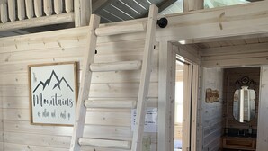 A wooden interior with a white ladder, a framed quote on the wall, and a bathroom visible through an open door.