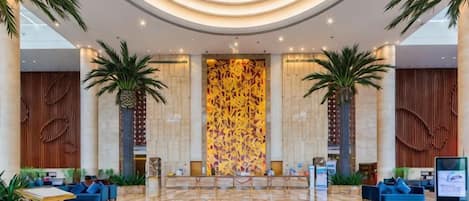 A spacious lobby with a central reception desk, seating areas, and a decorative wall.