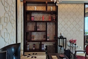 Una habitación con una estantería de madera oscura llena de libros y objetos decorativos, un sillón de cuero negro, una mesa de comedor con un mantel rojo y un papel tapiz estampado.