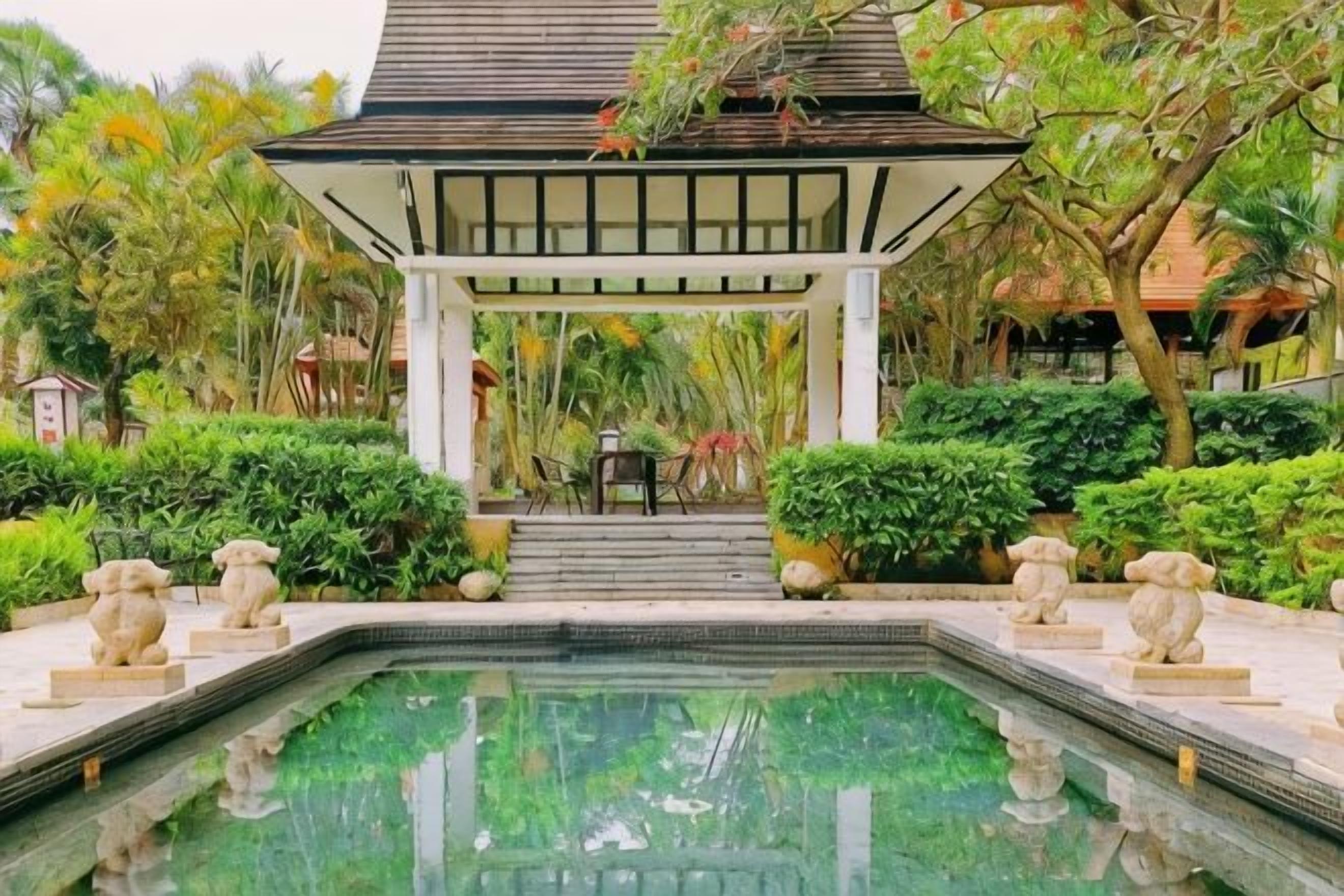 Un espace piscine agrémenté d’un gazebo, de marches menant à une table et de sculptures en pierre.