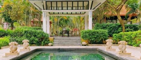 A pool area with a gazebo, steps leading to a table, and stone sculptures.