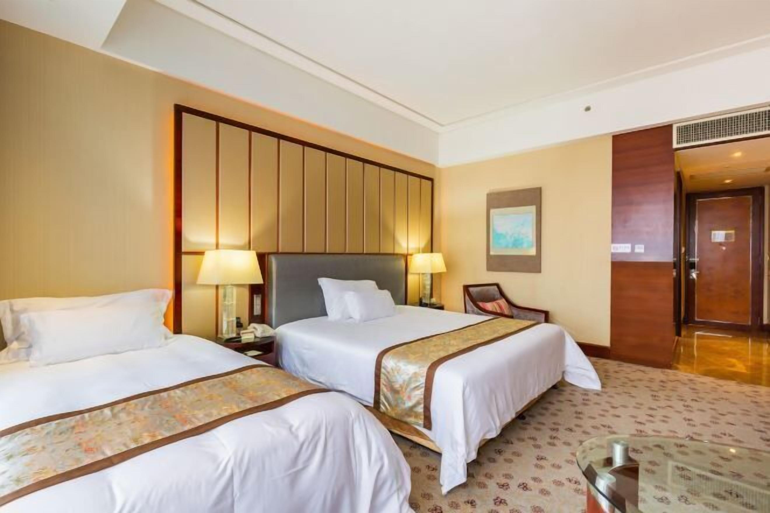 A hotel room with two beds, a large wooden headboard, a desk with a chair, and a small table.