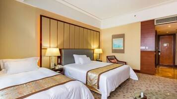 A hotel room with two beds, a large wooden headboard, a desk with a chair, and a small table.