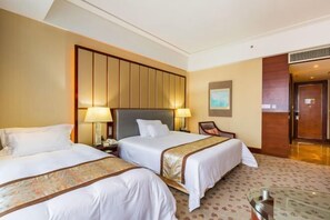 Habitación de hotel con dos camas, un gran cabecero de madera, un escritorio con una silla y una mesita.