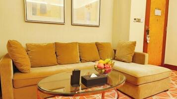 Una sala de estar con un sofá beige, una mesa de centro de vidrio y un frutero. Hay dos cuadros en la pared y una puerta con cerradura.