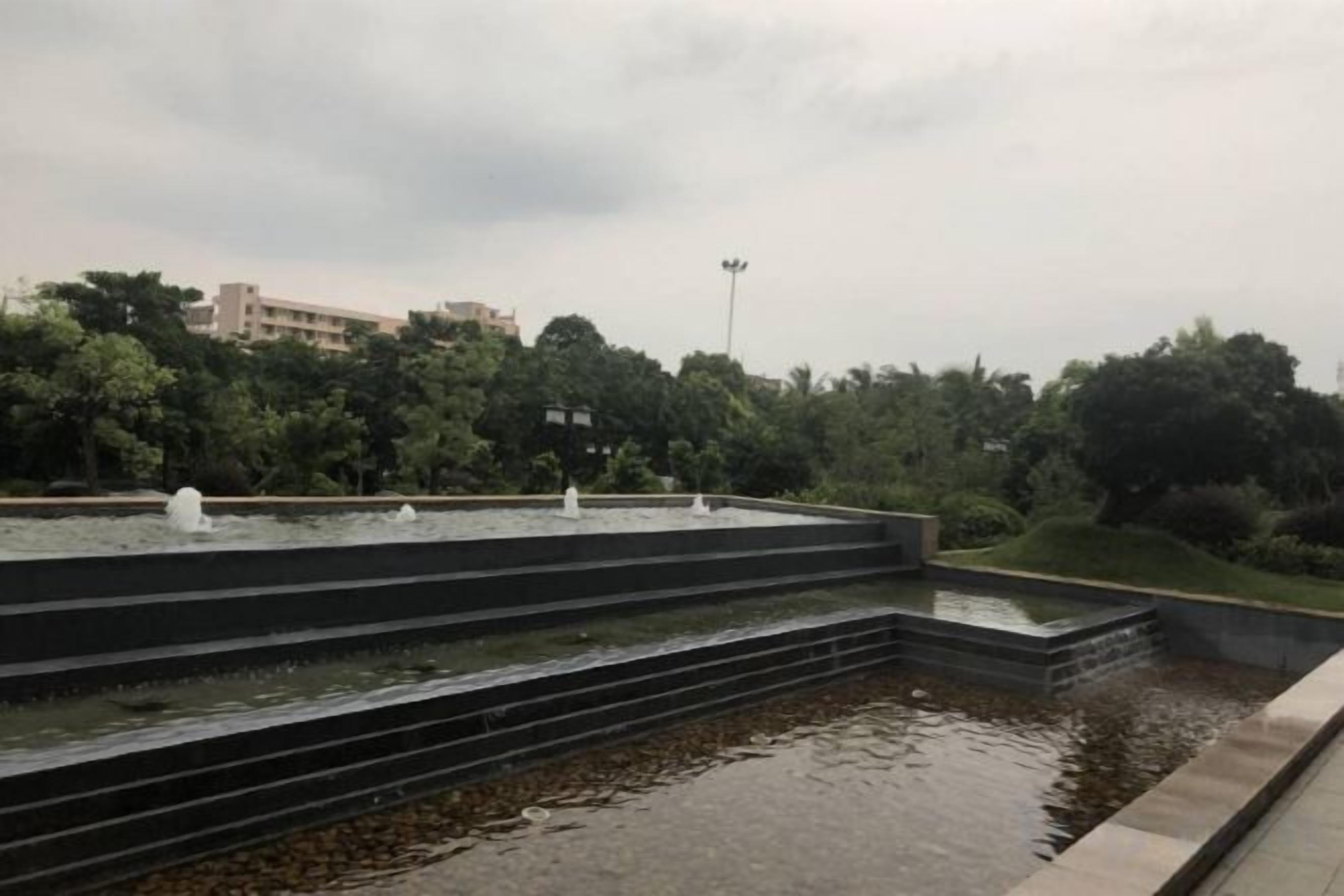 A tiered water feature with multiple fountains, surrounded by a landscaped garden and trees.