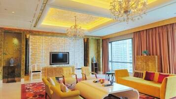 A spacious living room with a large TV, yellow sofas, and a chandelier.