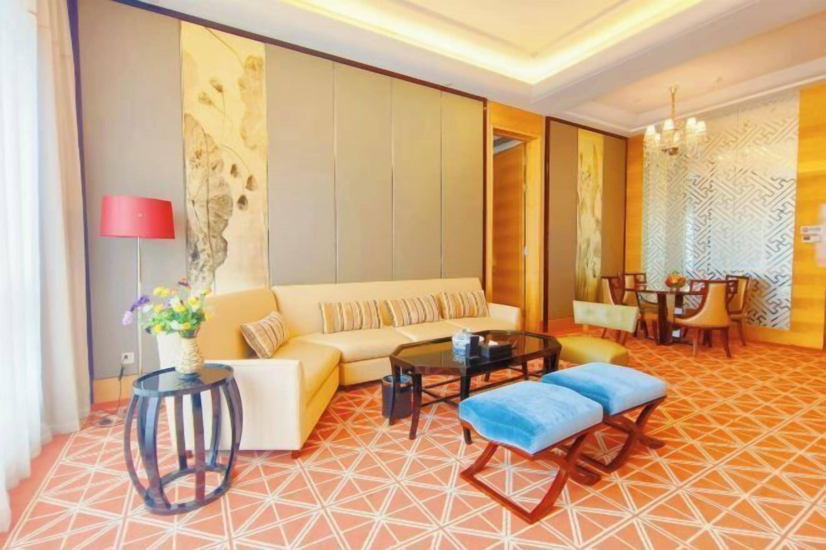 A modern living room with a sofa, coffee table, and ottoman, a dining area with chairs, and a patterned floor.