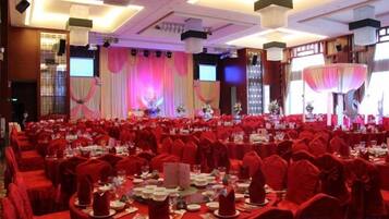 A banquet hall with round tables, red chairs, and a stage with curtains.