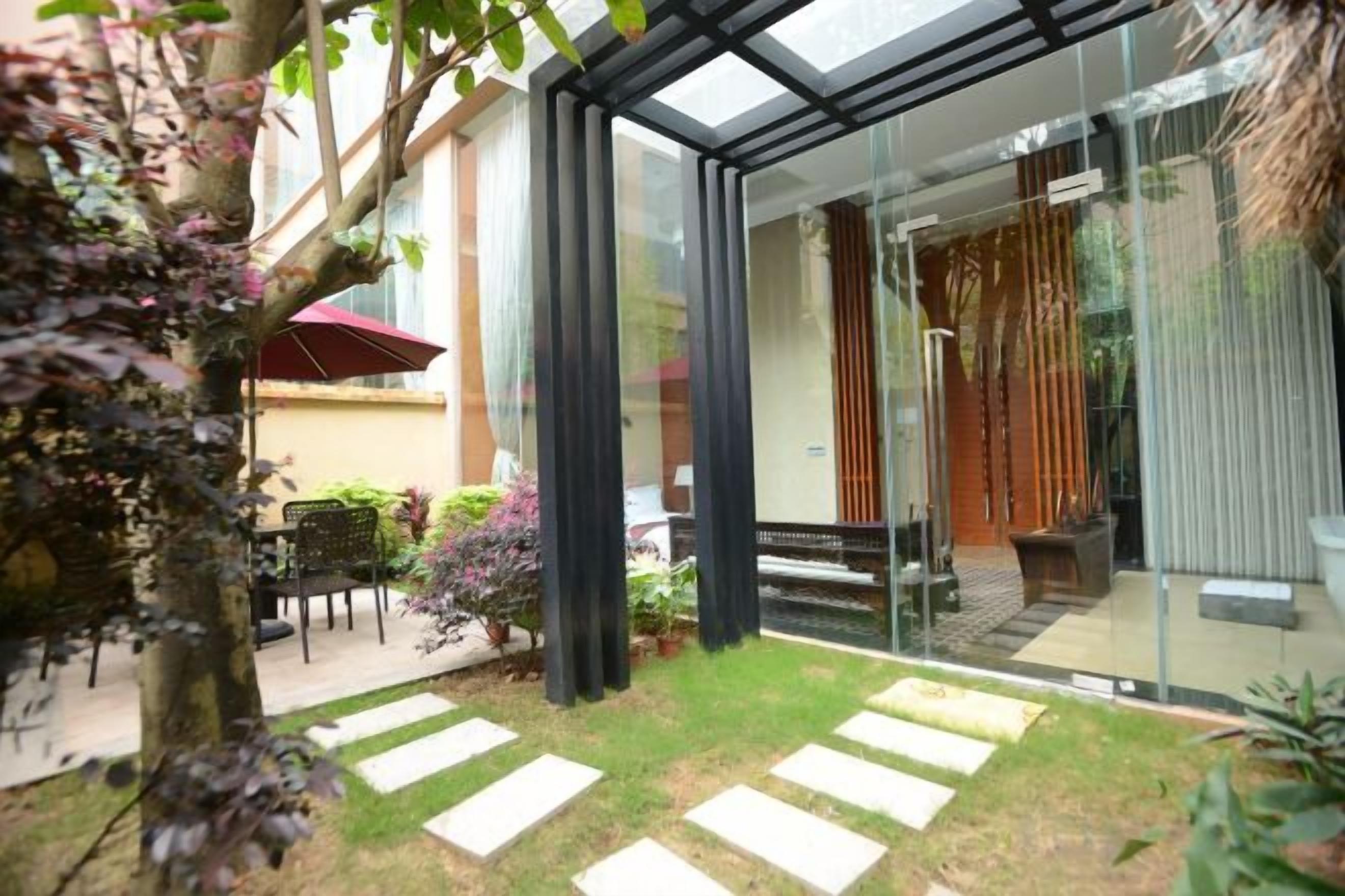 Una casa moderna con puerta de vidrio que da a un patio, un jardín pequeño y un conjunto de asientos.