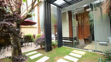 Una casa moderna con puerta de vidrio que da a un patio, un jardín pequeño y un conjunto de asientos.