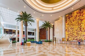 A spacious lobby with a high ceiling, palm trees, and a large patterned wall. - Lotin Hot Springs Hotel (Gaozhou)