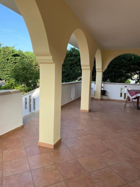 Un patio extérieur couvert, doté d’un sol carrelé et d’une table dressée pour les repas.