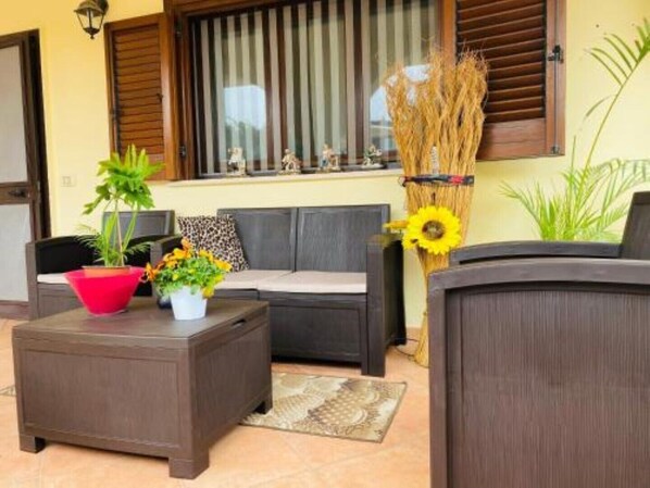 A cozy outdoor seating area with a dark brown sofa, a small side table with a red pot and a white pot, and a decorative sunflower arrangement.