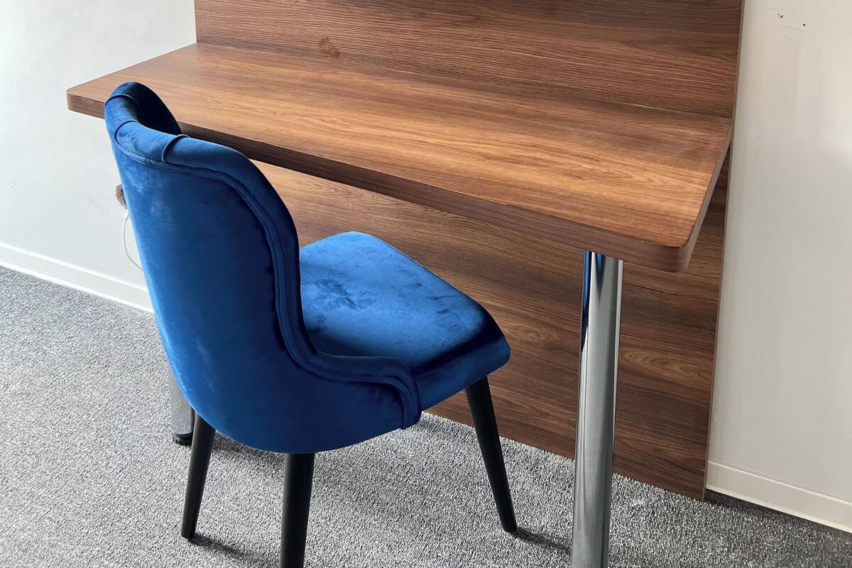 Una habitación moderna con un escritorio de madera, una silla azul y un televisor de pantalla plana montado.