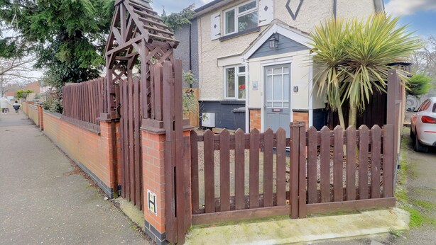 A residential property with a gated entrance, a brick wall, a wooden fence, and a house with a tiled roof and a window with shutters.
