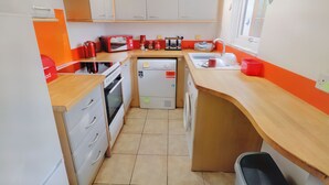 A compact kitchen with white cabinets, a wooden countertop, a built-in oven, a washing machine, and a small sink.