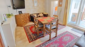 A living room with a wooden dining table, leather sofa, and a TV mounted on the wall.