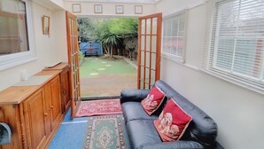 A cozy room with a black leather sofa, wooden cabinet, and a glass door leading to a garden.