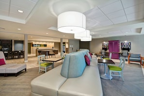 A modern lounge area with a sofa, chairs, a dining table, and a kitchen in the background. - Home2 Suites By Hilton Livermore (Livermore)
