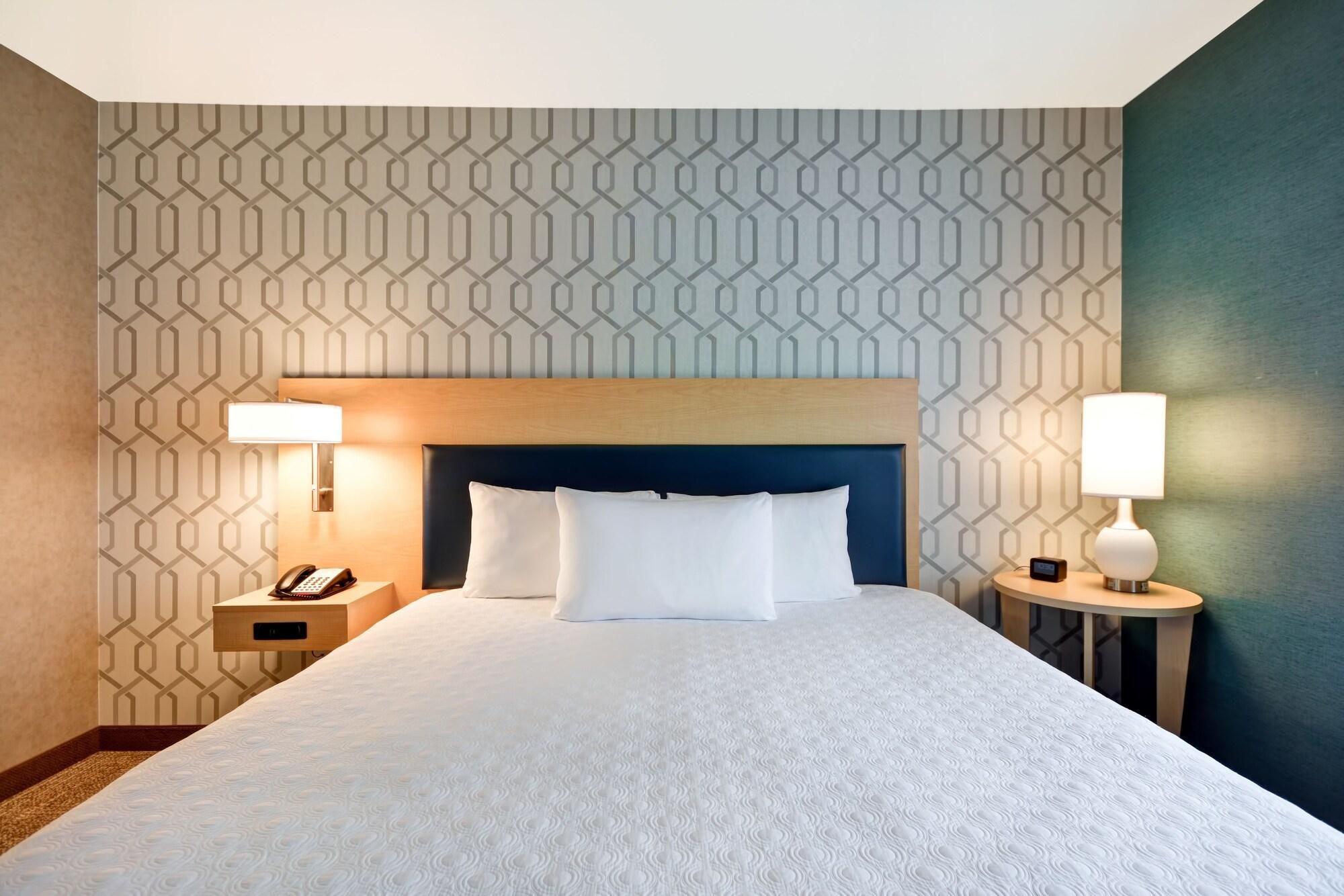 A hotel room with a large bed, two bedside tables, a headboard, and patterned wallpaper.
